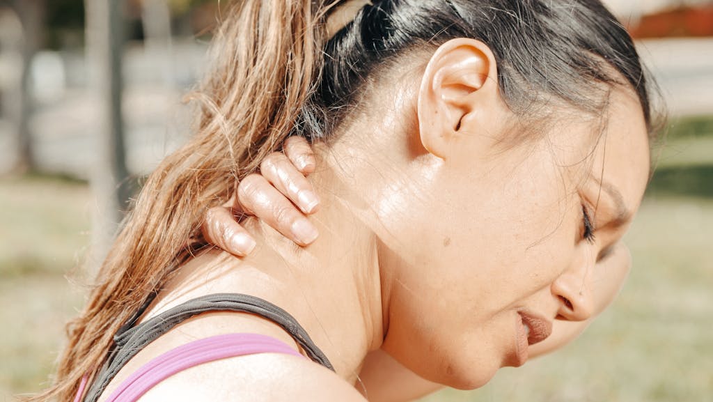 Close-up of a woman holding her neck, showing discomfort and pain outdoors.